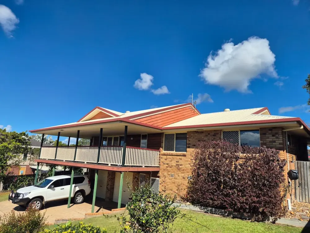 Two-storey brick home with an orange metal roof and balcony